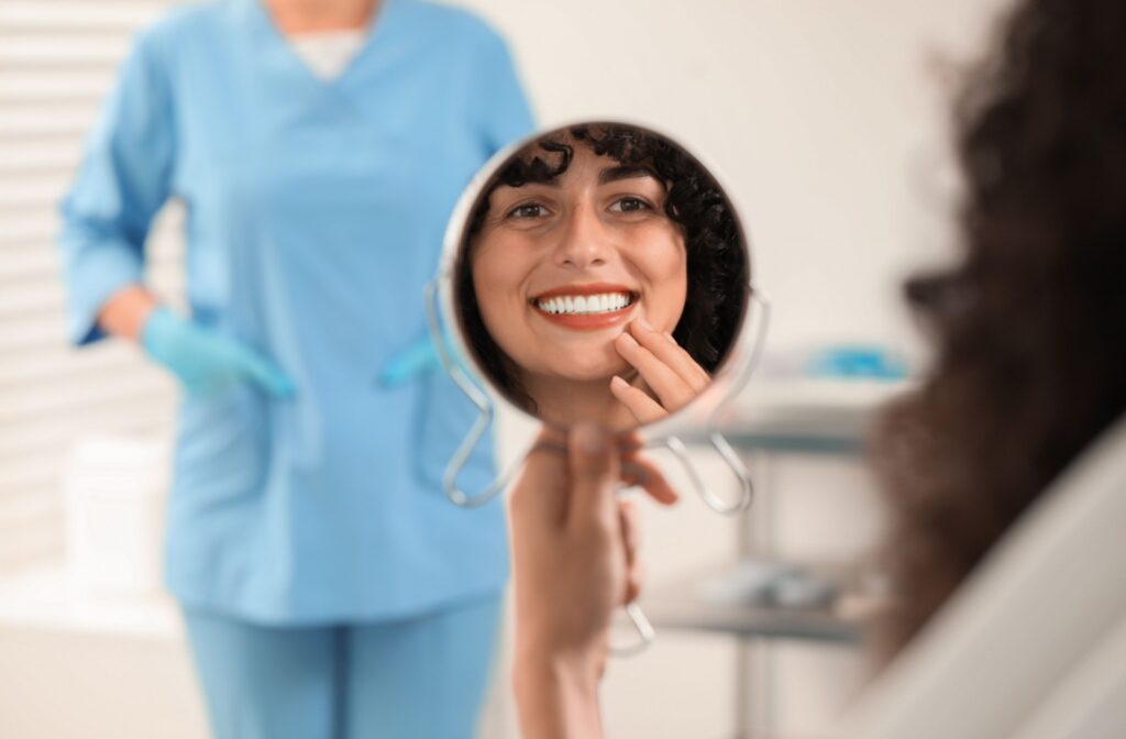 A dental patient looking in a handheld mirror smiling after getting a dental crown treatment.
