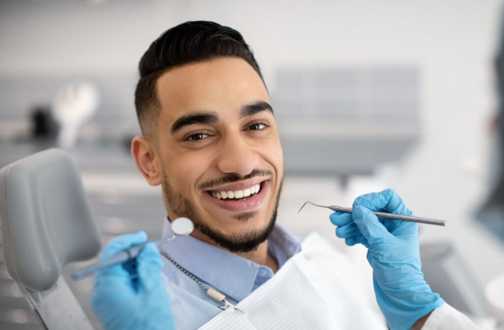 A dental patient smiling at the camera while the dental professional holds up dental tools