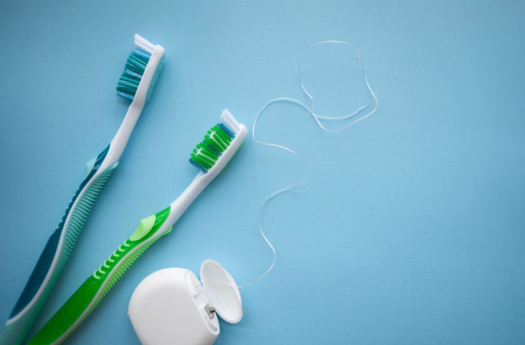 Two toothbrushes and floss on a blue surface.